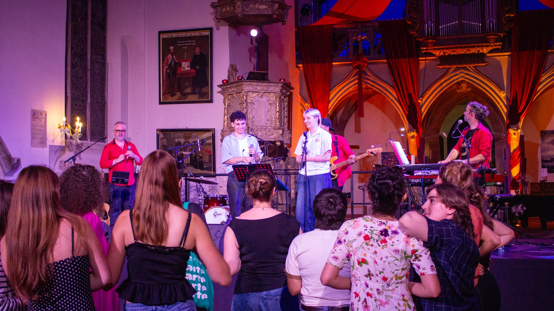 Concert dans une salle illuminée de violet, public au premier rang