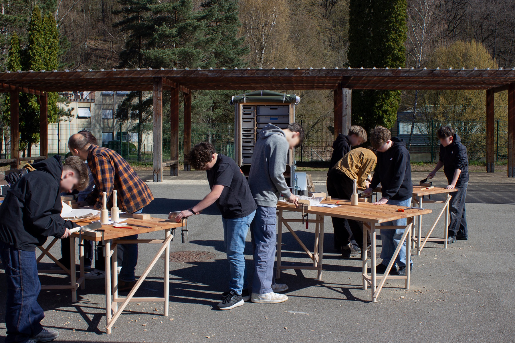 Artisans et participants travaillant le bois sur des établis en plein air, Atelier Dubois